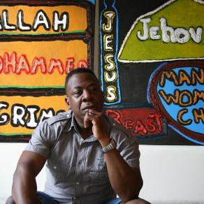 The artist Darrell Black sitting in front of his two expressions of faith